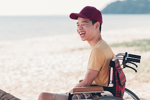 Teenage boy in wheelchair and with mental disability smiling at someone off camera.